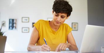 une femme regarde un e-learning devant son ordinateur portable et prend des notes